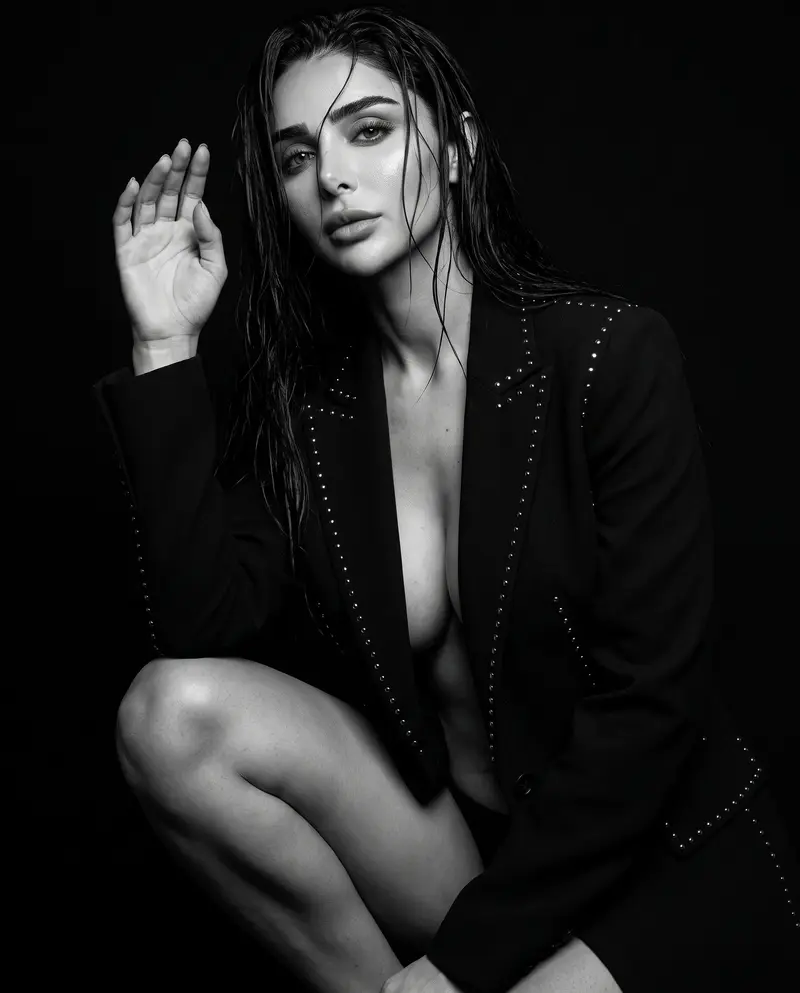 Crouched pose in a studded black jacket, one hand raised against the dark