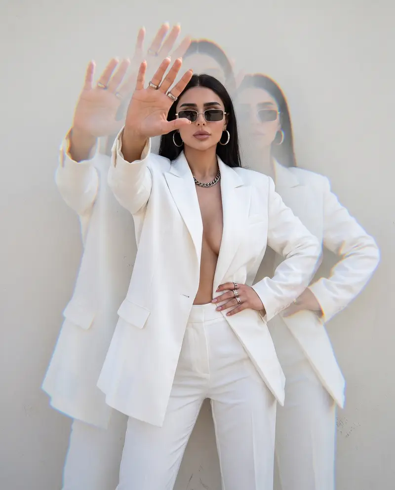 White suit against a white wall, hand raised to the lens, prism ghosting